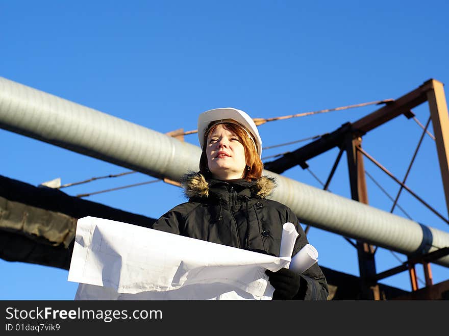 Young architect looking at blueprint in front of construction site against blue sky. Young architect looking at blueprint in front of construction site against blue sky