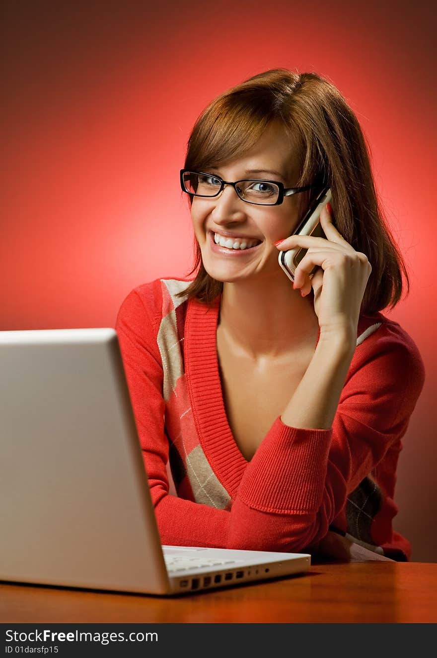 Beautiful smiling woman working on her laptop and talking on cell phone