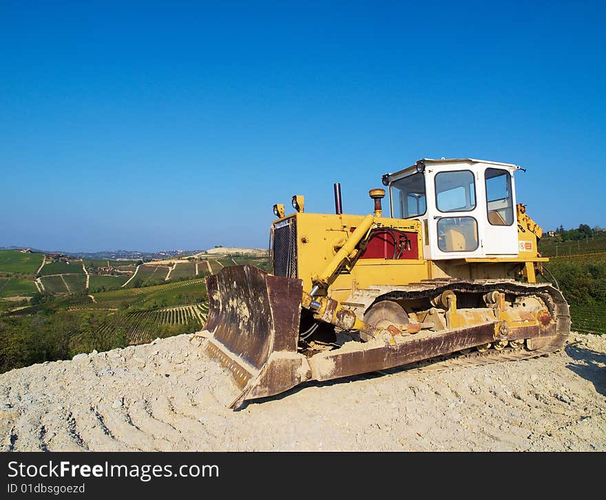 An excavator on the Langhe hills, full of green vineyards, Piedmont, Italy. An excavator on the Langhe hills, full of green vineyards, Piedmont, Italy.