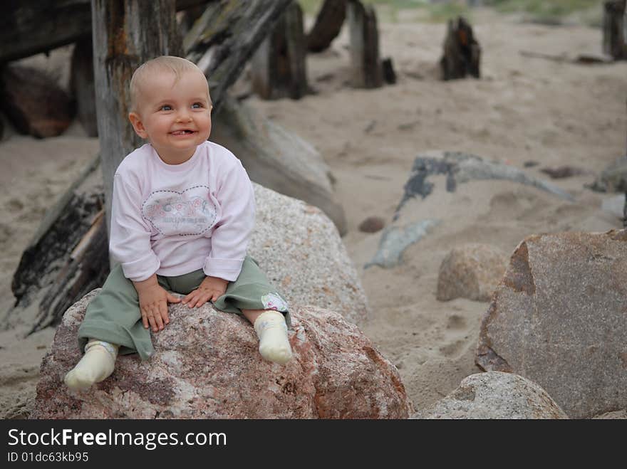 Beautiful child sits on  stone at  sea. Beautiful child sits on  stone at  sea