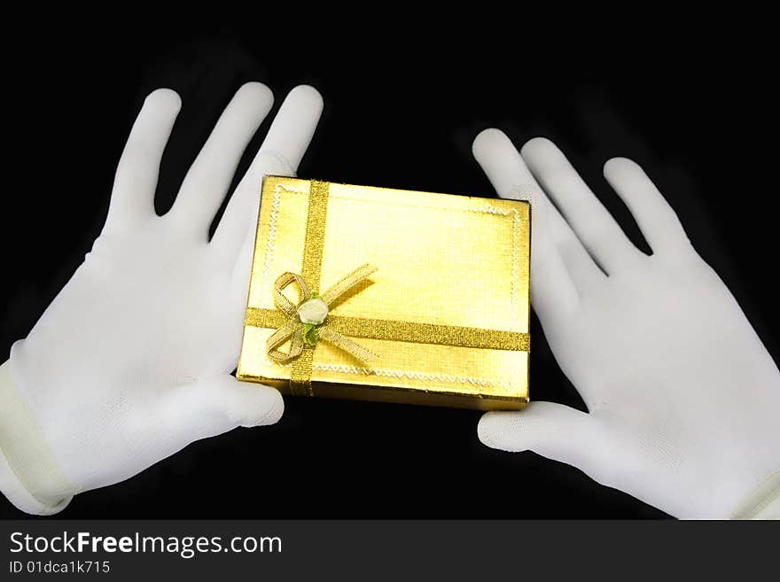 Hands in white gloves with a golden gift on a black background