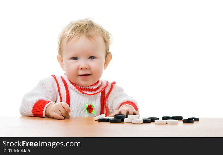 A little child sitting at a table with the heap of checkers lies on. A little child sitting at a table with the heap of checkers lies on