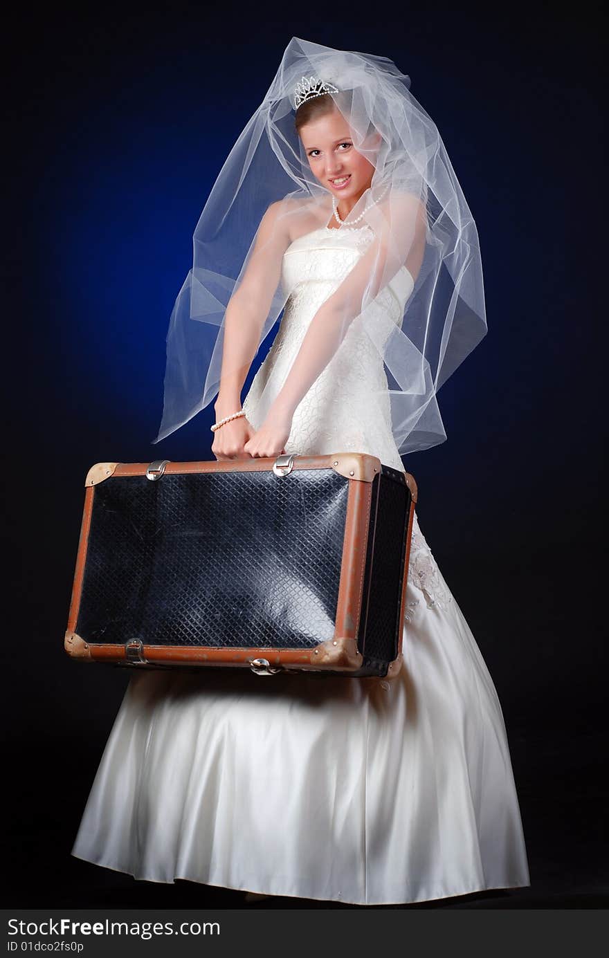 Young bride with heavy travelling bag on a black background