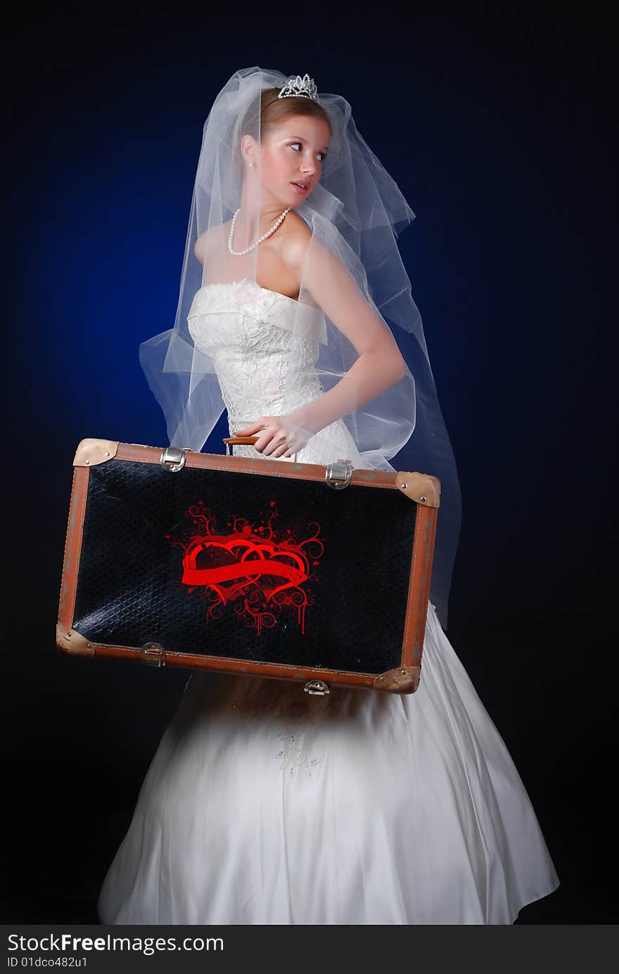 Young bride with heavy travelling bag on a black background