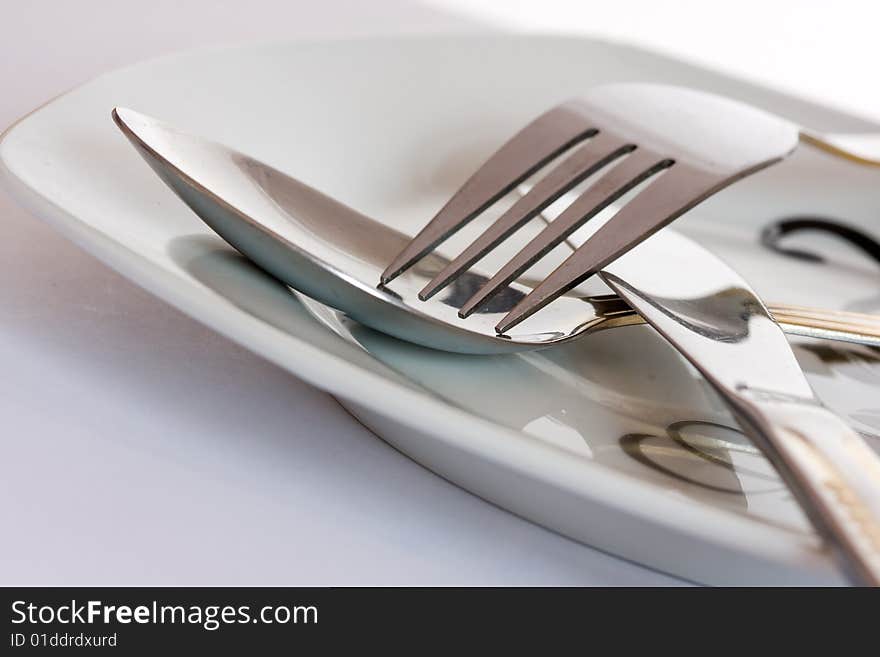 Detail of fork and spoon on white plate. Detail of fork and spoon on white plate