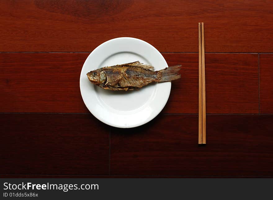 Fried crucian  in white plate with chopsticks on wooden tabie