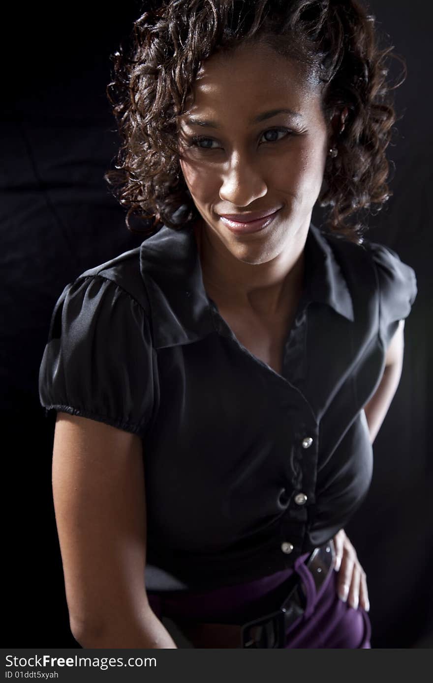 Young adult black woman with smile while leaning forward, backlit on black background. Young adult black woman with smile while leaning forward, backlit on black background.