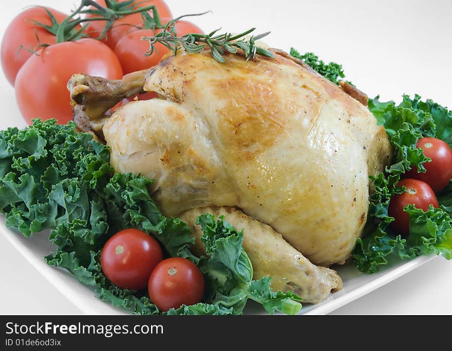 Whole roasted chicken garnished with kale, cherry tomatoes, and rosemary