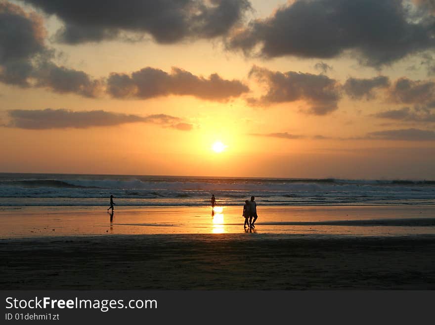 Sun setting over a sandy beach in Bali. Silhouettes of people walking. Sun setting over a sandy beach in Bali. Silhouettes of people walking