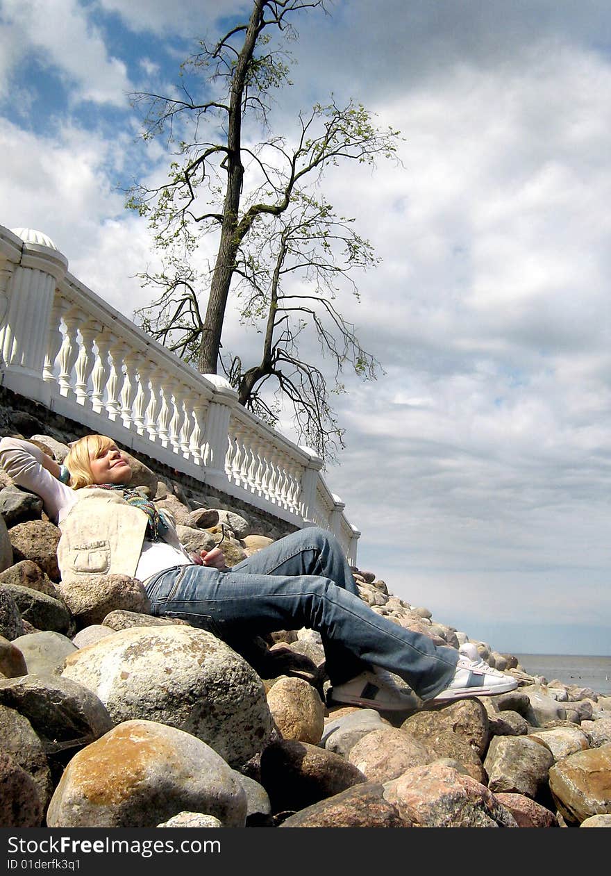 Happy girl on the stones near tree and with sea view