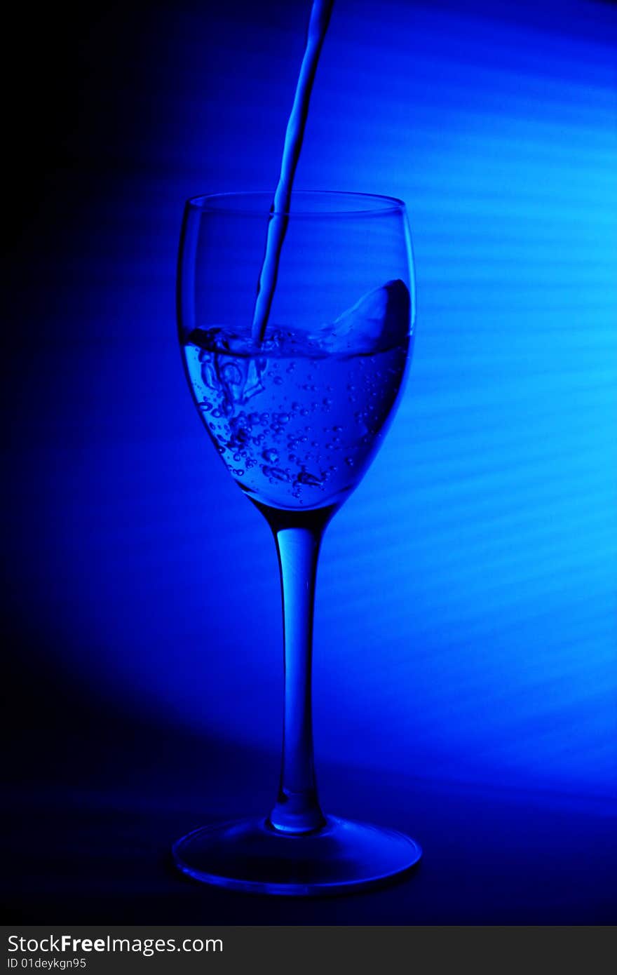 A glass of water being poured intoa wine glass with a blue background. A glass of water being poured intoa wine glass with a blue background.