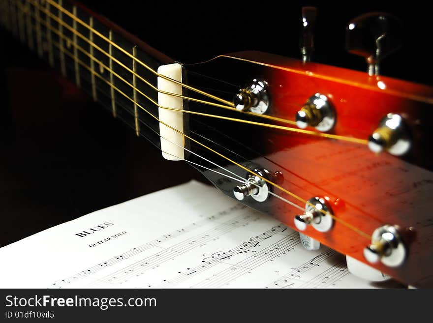 Guitar headstock and tuning pegs closeup against a blues sheet music in the darkness