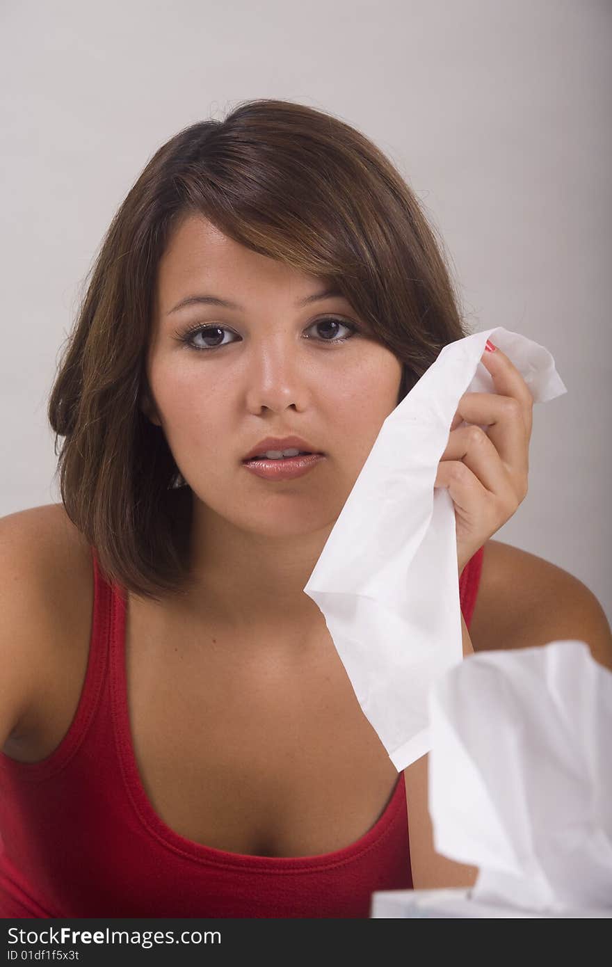 A young Asian girl with a cold blows her nose into a tissue. A young Asian girl with a cold blows her nose into a tissue