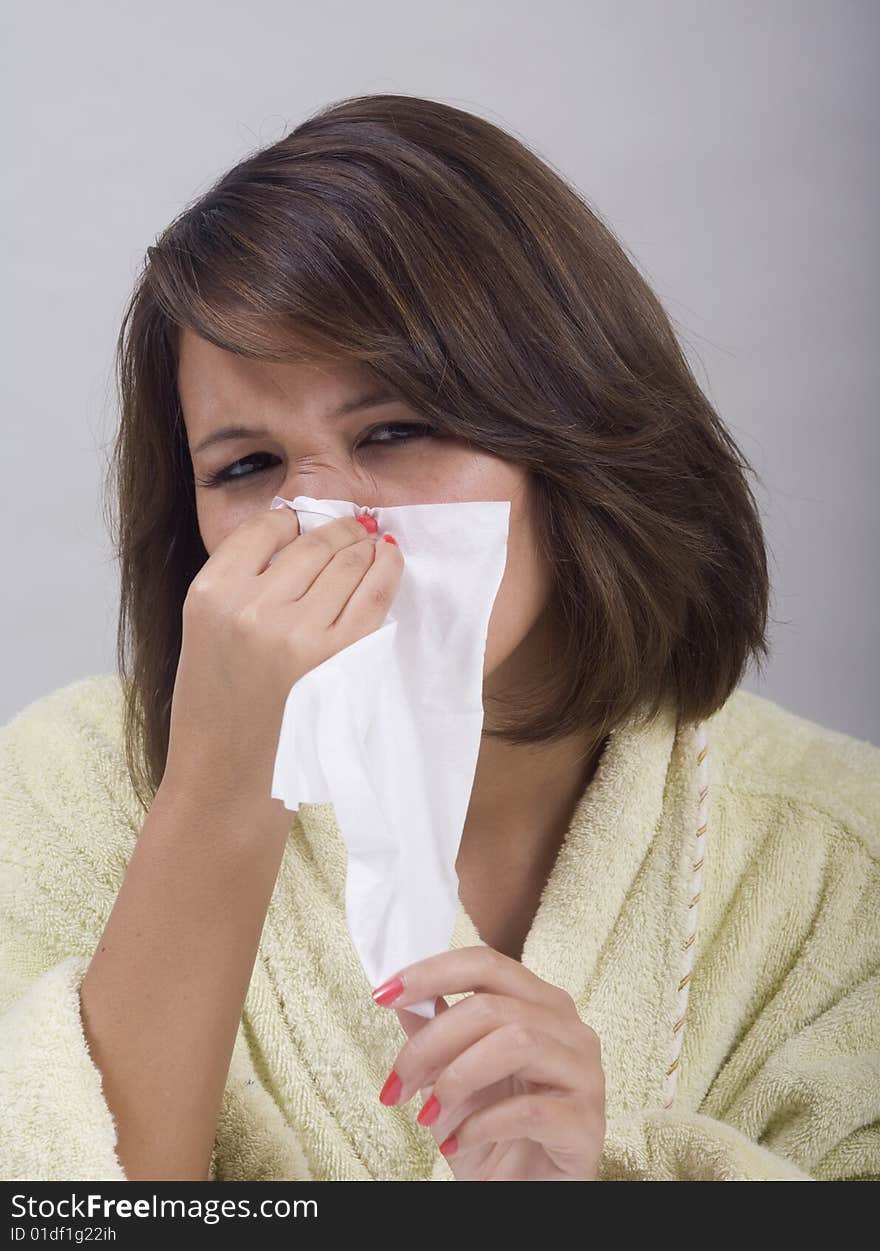 A young Asian girl with a cold blows her nose into a tissue. A young Asian girl with a cold blows her nose into a tissue