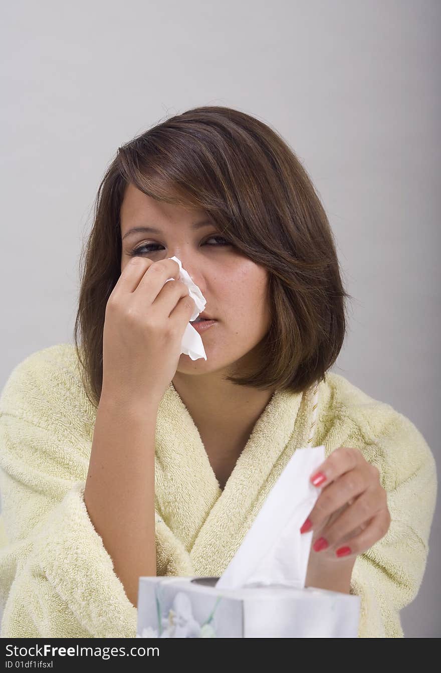 A young Asian girl with a cold blows her nose into a tissue. A young Asian girl with a cold blows her nose into a tissue