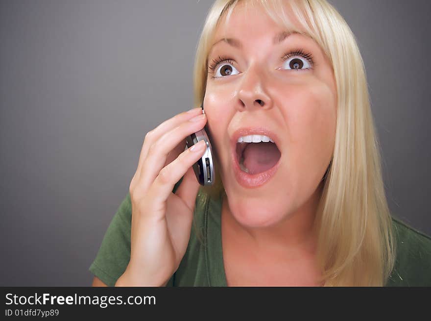 Stunned Blond Woman Using Cell Phone Against a Grey Background.