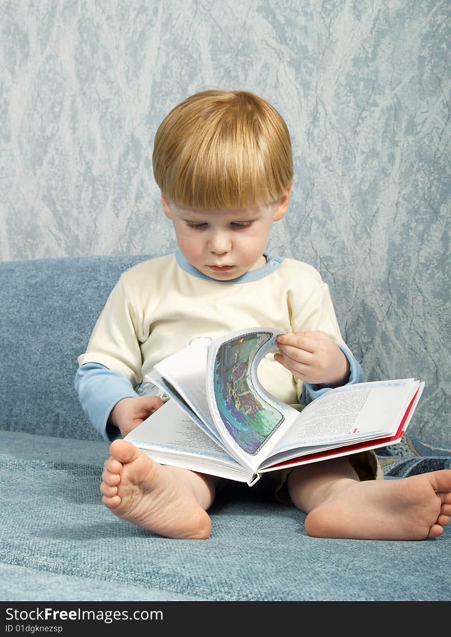 The little boy with the book sitting on a sofa. The little boy with the book sitting on a sofa