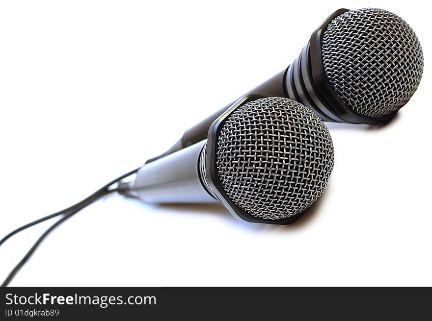 Two black wired karaoke microphones with gray metal grill on isolated background. Two black wired karaoke microphones with gray metal grill on isolated background.