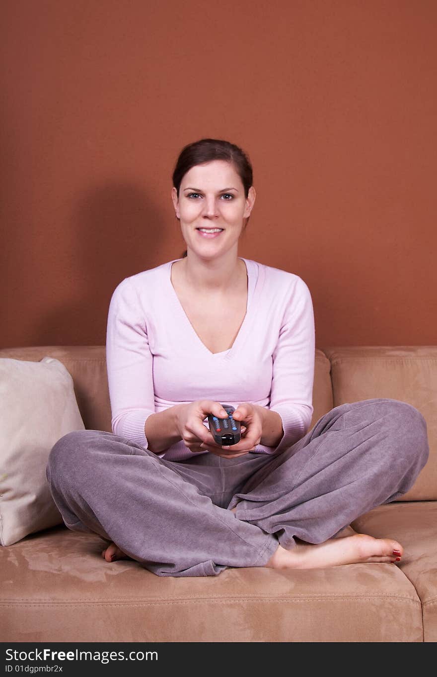 A young woman sits in front of a TV with the remote control in her hand on a couch. A young woman sits in front of a TV with the remote control in her hand on a couch.