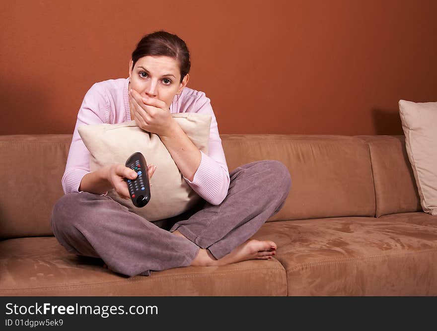 A young woman sits in front of a TV with the remote control in her hand on a couch. A lot of copyspace left. She seems to be afraid. A young woman sits in front of a TV with the remote control in her hand on a couch. A lot of copyspace left. She seems to be afraid.