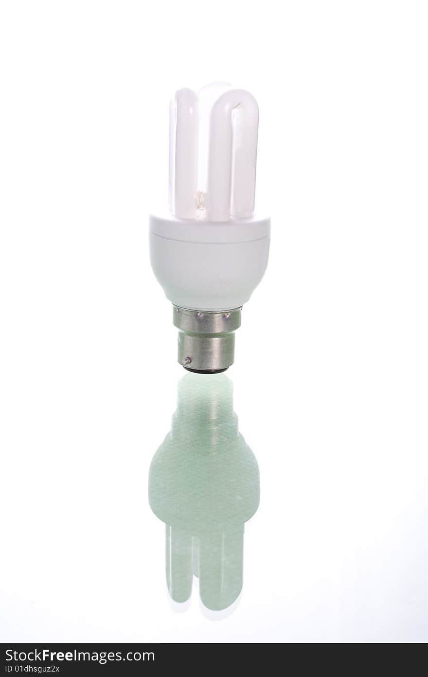 A single energy bulb on reflective surface against white. A single energy bulb on reflective surface against white