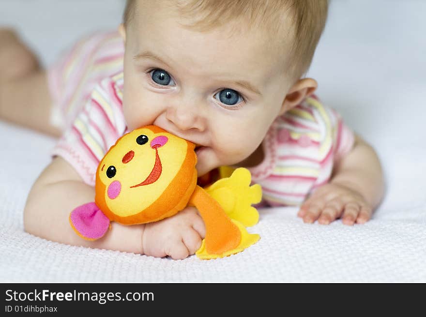 Little girl laying on a white bed playing with a toy monkey. Little girl laying on a white bed playing with a toy monkey