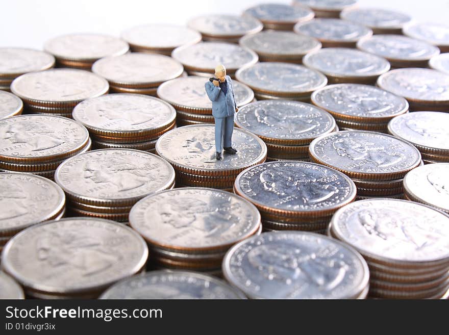 Miniature businessman on a cell phone standing on quarters. Miniature businessman on a cell phone standing on quarters.