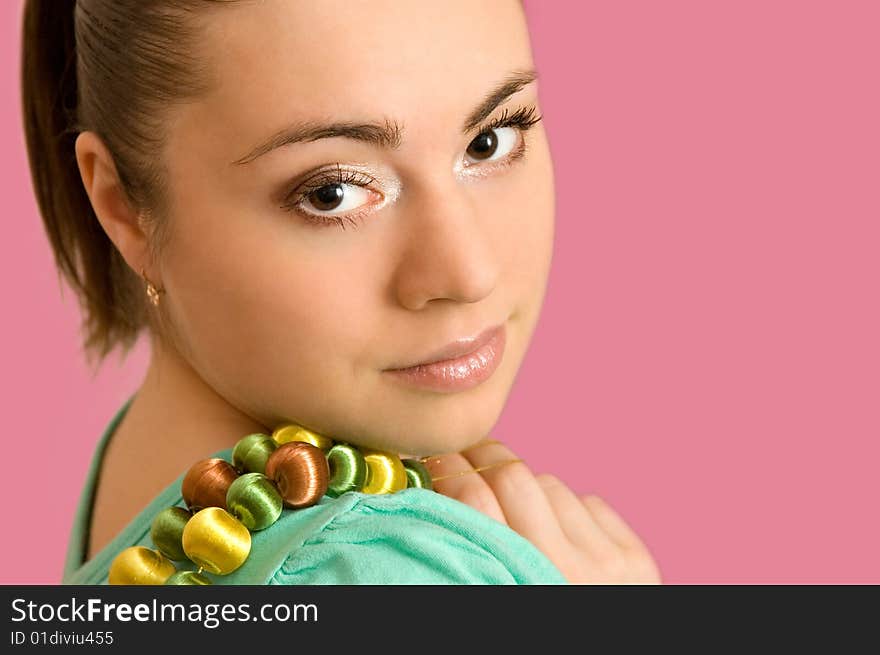 The beautiful young woman with a beads on a pink background