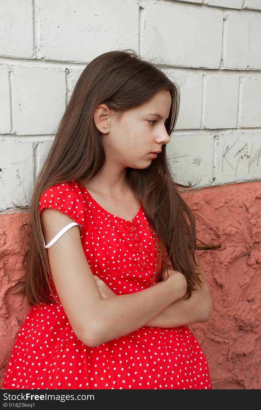 Beautiful sad girl in red dress  in front of brick wall. Beautiful sad girl in red dress  in front of brick wall