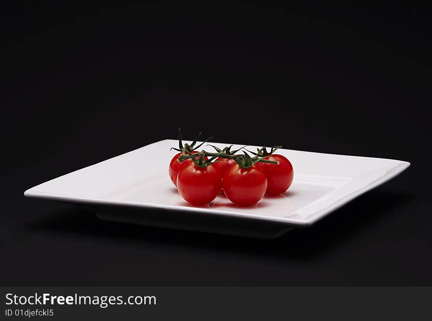 Five cherry tomatoes on a white plate with black background.