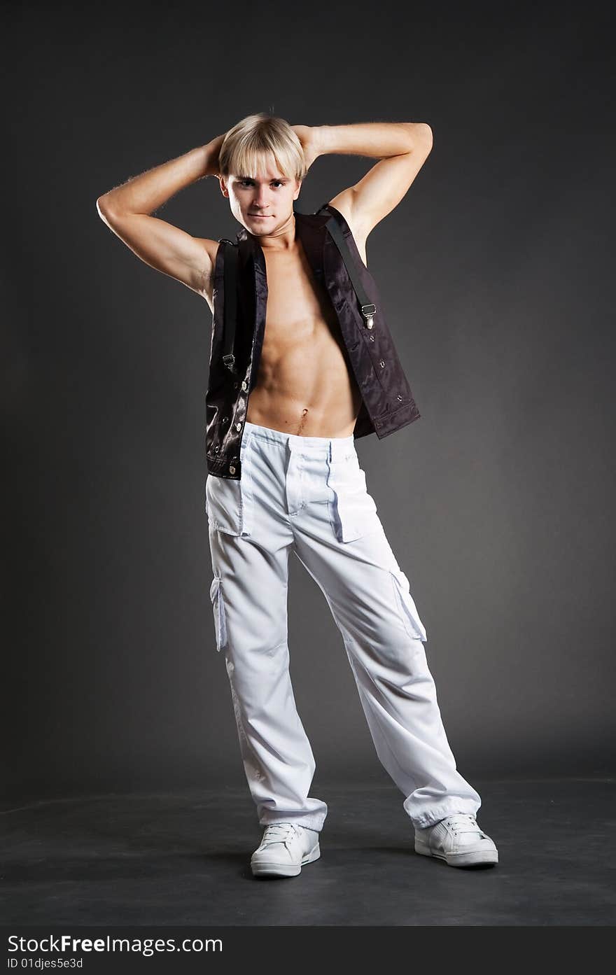 Young dancer in white trousers posing over dark background