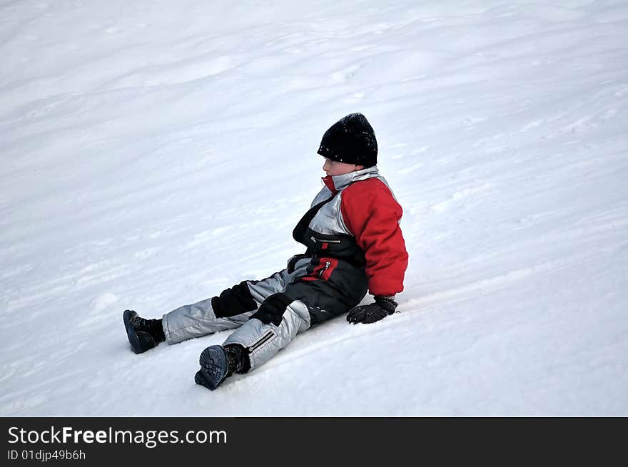 A boy slipped and sits on the snow