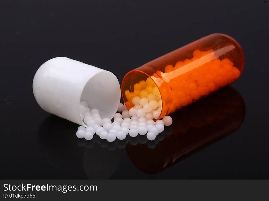 Close-up of a capsules of medication. It has been opened and the contents have spilled out. Black background.