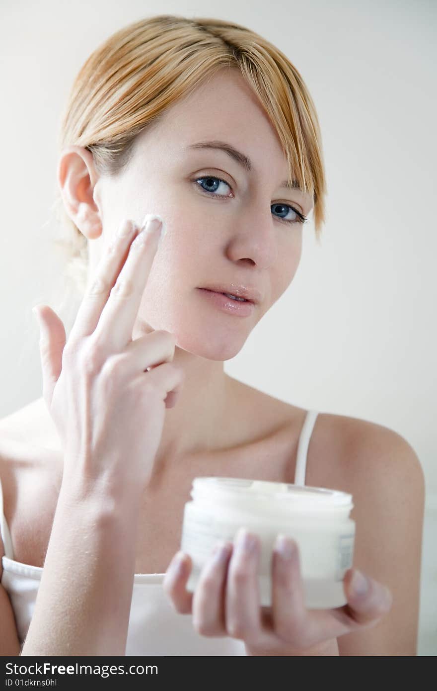 Young woman applying cream on her face. Young woman applying cream on her face.