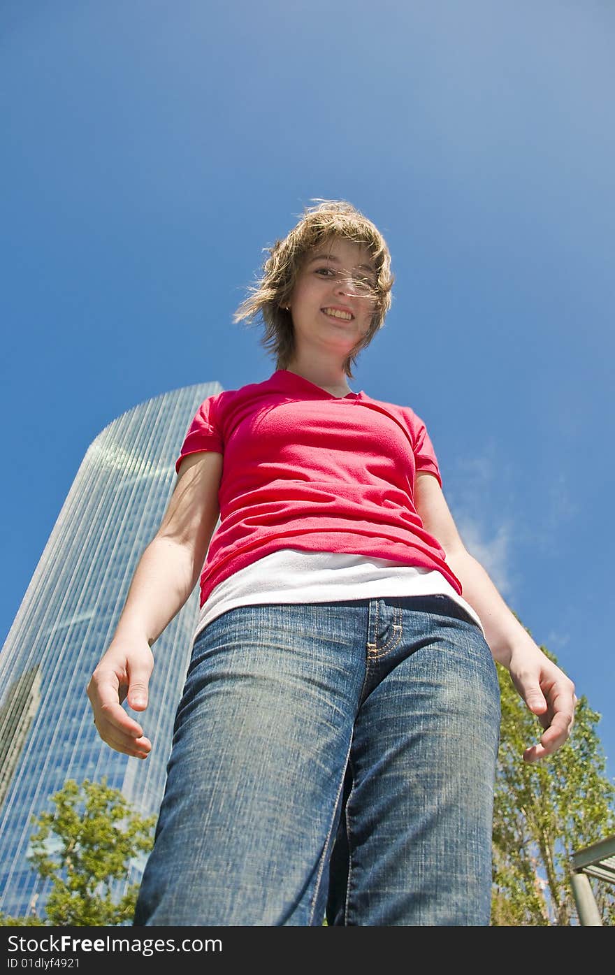 Portrait of a teen girl in casual clothing taken from a low angle with a modern building, trees and a blue sky in the background. Portrait of a teen girl in casual clothing taken from a low angle with a modern building, trees and a blue sky in the background