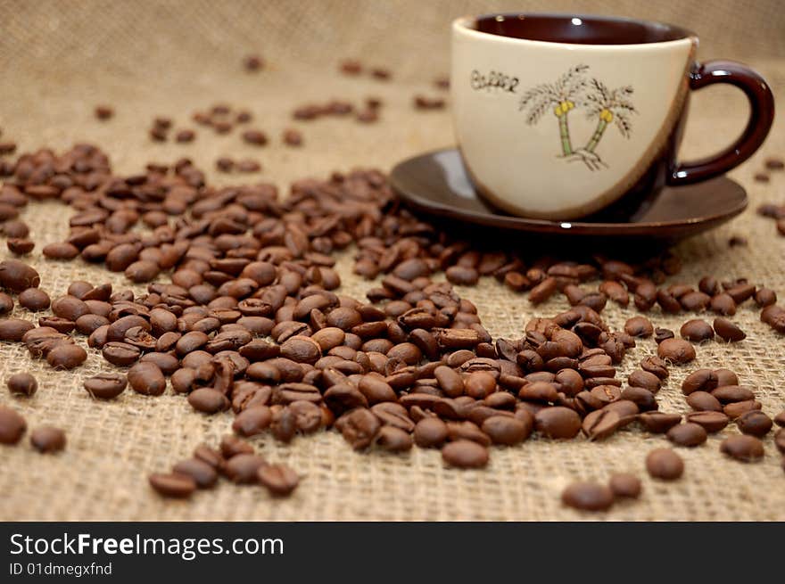 Coffee beans on focus and cup with cofee at the background. Coffee beans on focus and cup with cofee at the background