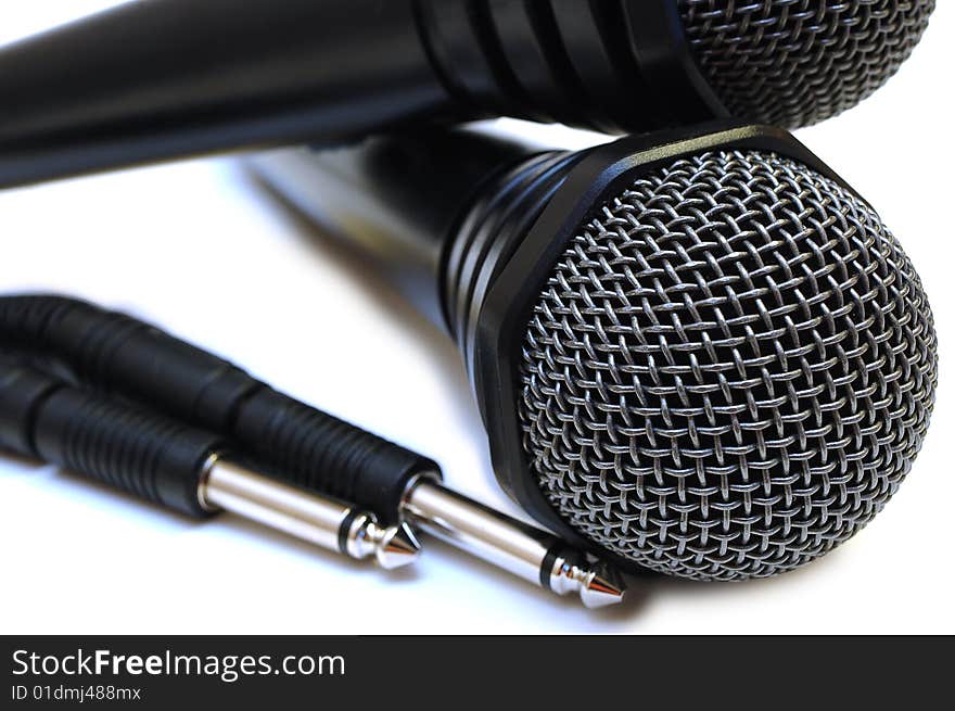 Two black wired karaoke microphones with gray metal grill on isolated background. Two black wired karaoke microphones with gray metal grill on isolated background.