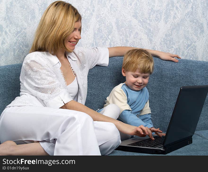 Young mum with the small beautiful boy together sit near laptop. Young mum with the small beautiful boy together sit near laptop