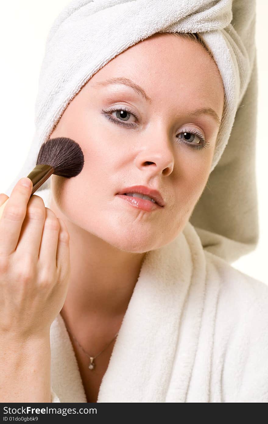 Attractive blond woman applying makeup wearing white robe and towel over head on white. Attractive blond woman applying makeup wearing white robe and towel over head on white