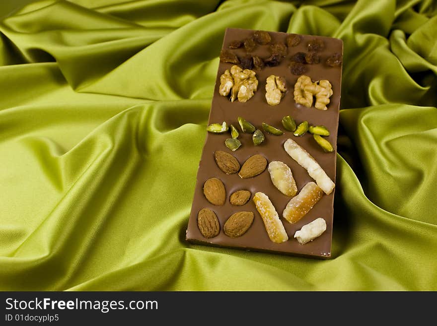 A chocolate - nougat bar with walnuts, almonds, raisins, pistachios and candied orange on green satin background. A chocolate - nougat bar with walnuts, almonds, raisins, pistachios and candied orange on green satin background.