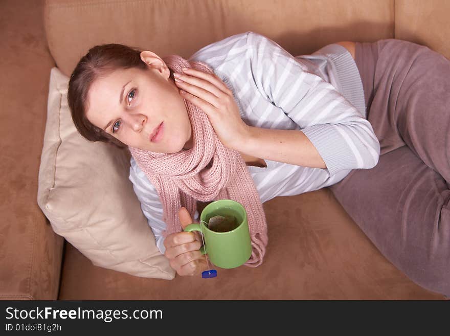 A young woman is sick. She is lying on the couch and is sneezing. She has a tea in her hand. A young woman is sick. She is lying on the couch and is sneezing. She has a tea in her hand.