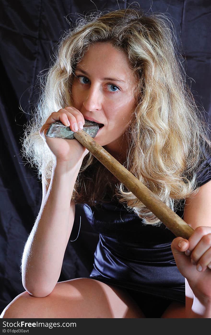 Young woman bites a hammer against a black background. Young woman bites a hammer against a black background