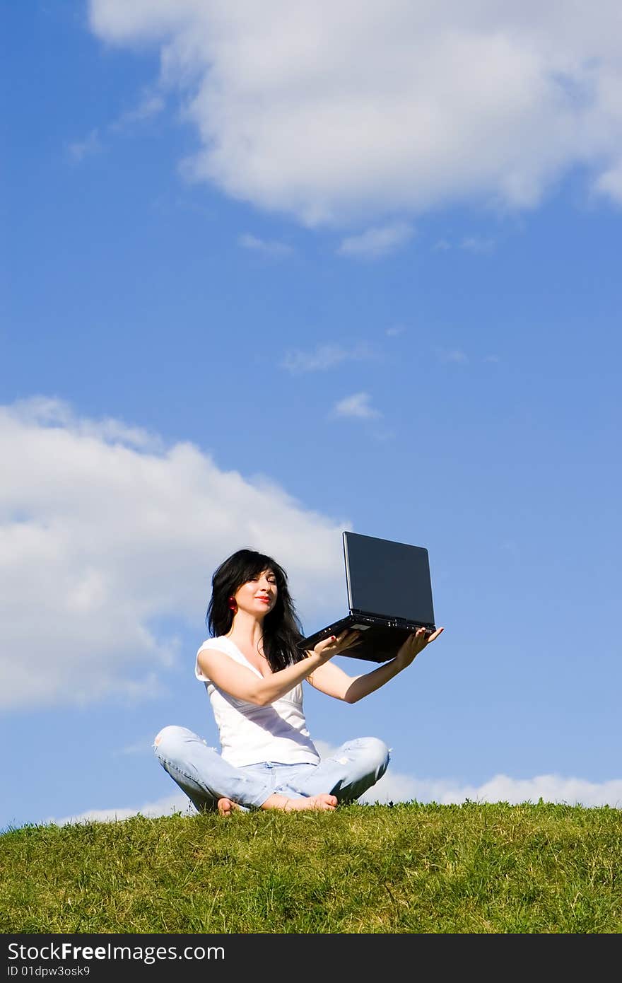 Pretty woman with laptop on the green grass