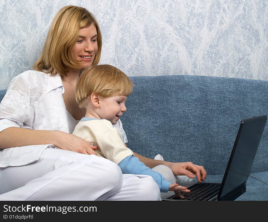 Young mum with the small beautiful boy together sit near laptop. Young mum with the small beautiful boy together sit near laptop