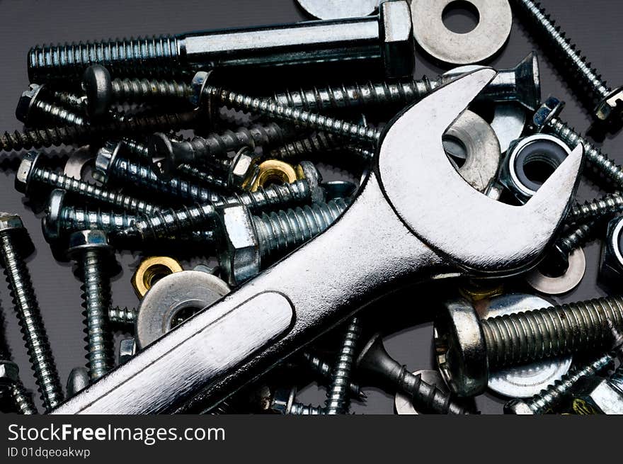 A close-up of various nuts, blots and screws and an open ended wrench on a black reflective surface