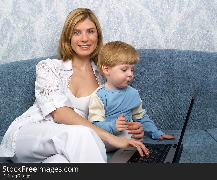 Young mum with the small beautiful boy together sit near laptop. Young mum with the small beautiful boy together sit near laptop