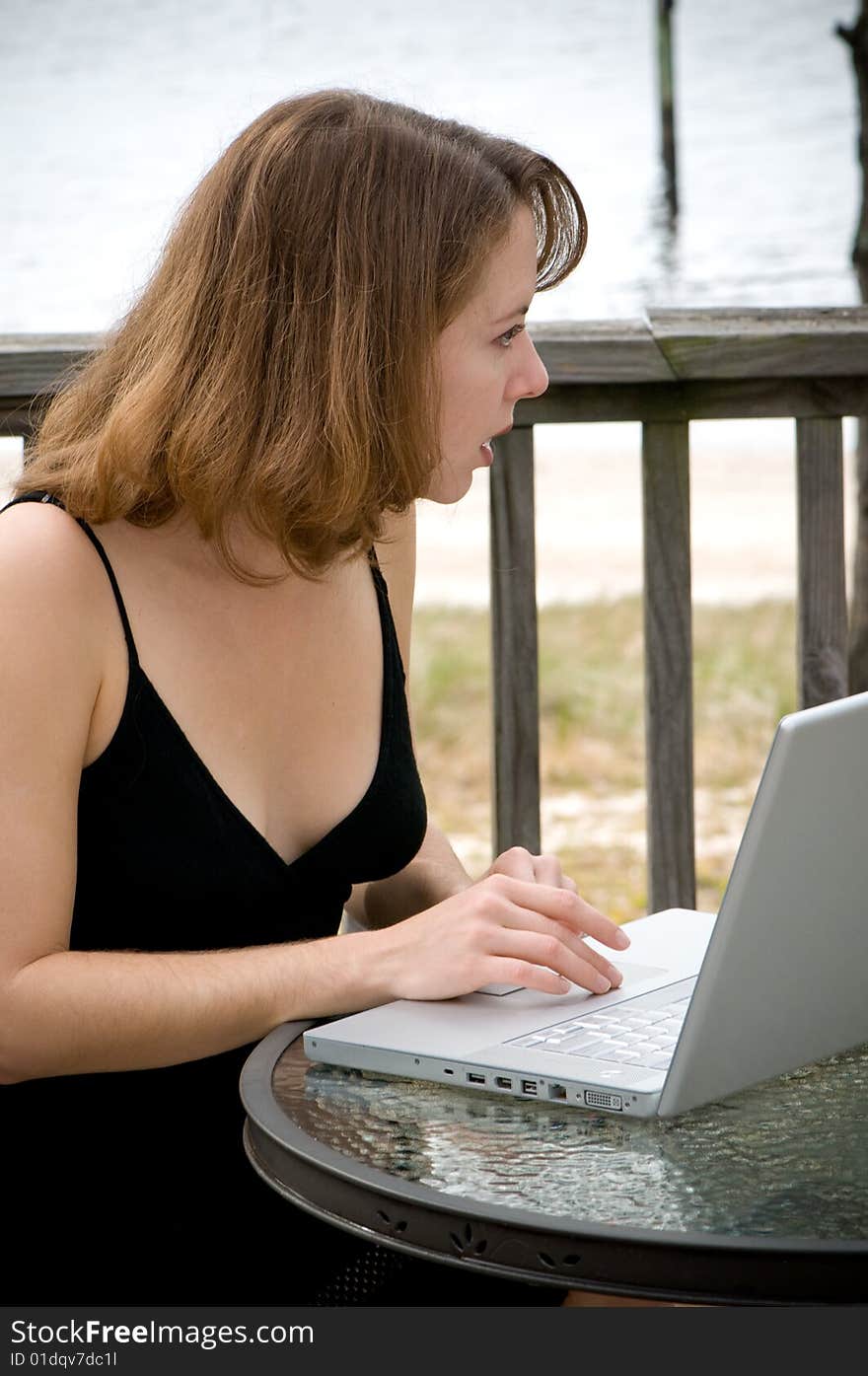 Young woman uses laptop on back deck of bayside home. Young woman uses laptop on back deck of bayside home.