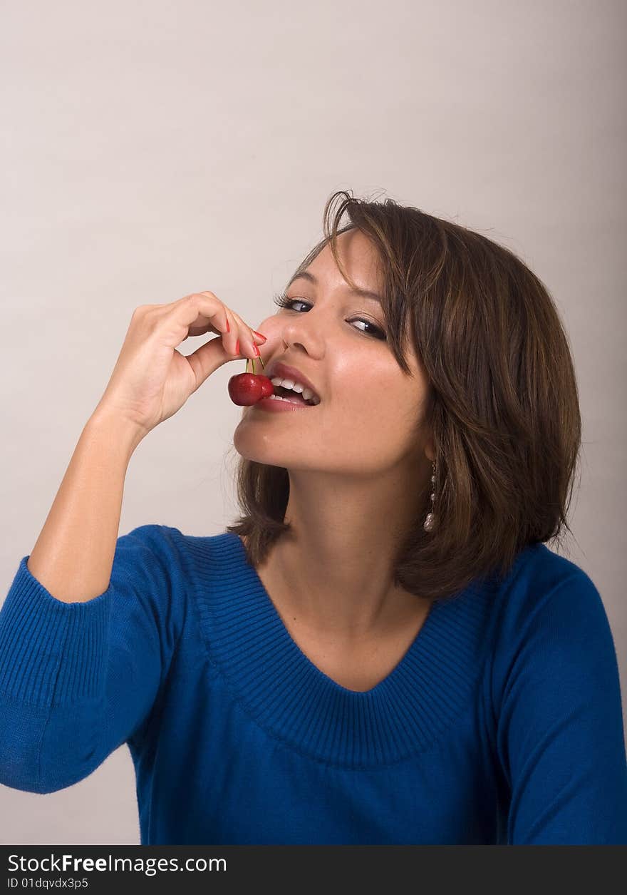 A beautiful young Asian-American girl eating red cherries