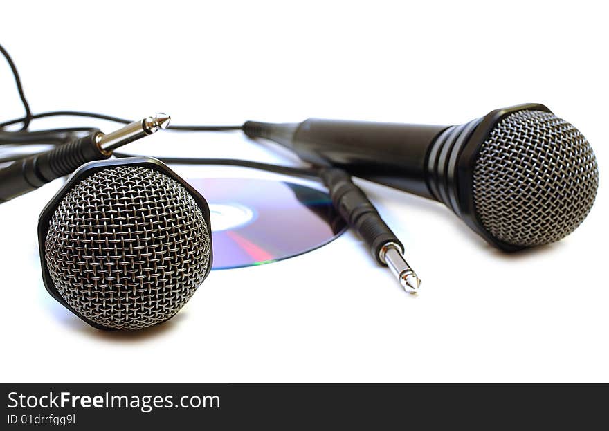 Two black wired karaoke microphones with gray metal grill on isolated background and CD (DVD) disk. Two black wired karaoke microphones with gray metal grill on isolated background and CD (DVD) disk.