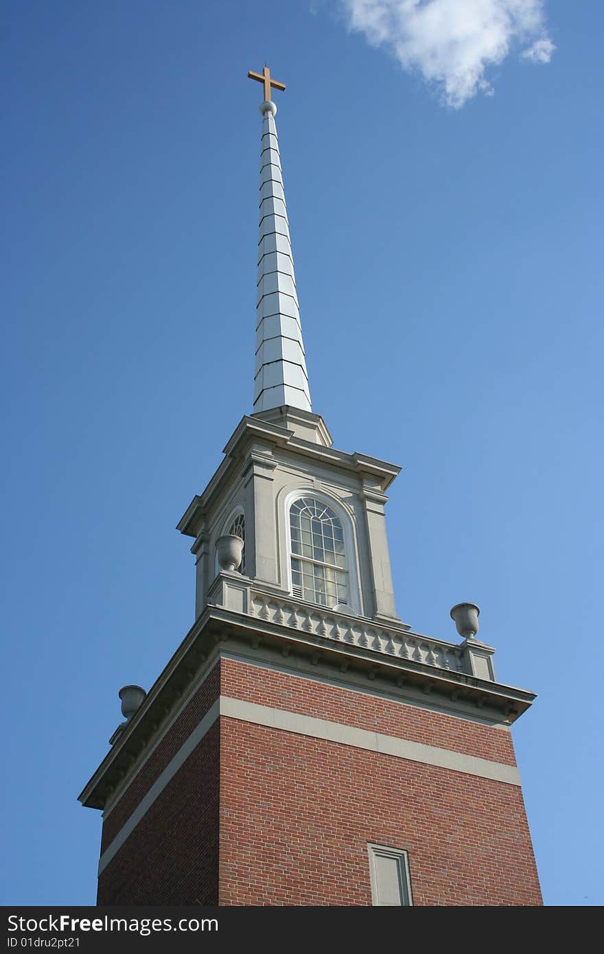 A traditional-style church steeple topped by a cross rises into a brilliant blue sky, with a few nice-day white clouds. Focus is on the steeple & cross. Includes copy space. Please use respectfully.